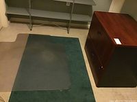 Photo showing wooden lateral file cabinet with two drawers and key on top, placed next to a carpet with large plastic office chair floor mat partially covering carpet.