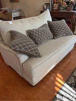 Front view of beige loveseat with back cushion and three decorative pillows