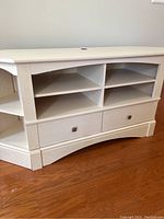 Front view showing the cabinet's open divided shelves, drawers with metal handles, and curved base design.