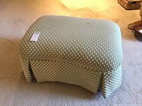 Front angle showing rectangular jacquard fabric covered ottoman with textured small dot pattern and skirted sides on a carpeted floor.