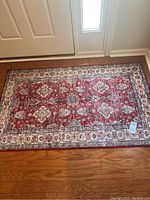 Full view of larger multi-color rug with red and cream floral-medallion pattern on wood floor near door.