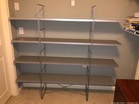 Full front view of shelving unit showing four horizontal shelves and metal frame supports on a carpeted floor in a small room.