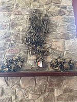 Three-piece faux metal floral wall art set displayed on stone wall with one large and two smaller panels.