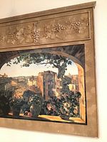 Front view of the wall art showing the Italian village scene through an arched opening with a grapevine motif on the top frame border.