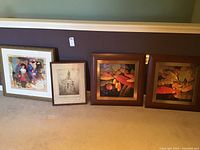 Four framed wall art pieces displayed on the floor against a wall, including two colorful prints, one antique etching, and one serigraph print with certificate of authenticity.