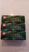 Three sleeves of Wilson Reflex Distance golf balls stacked horizontally, green boxes with white and red logo and text