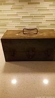 Closed antique metal fishing tackle box showing exterior condition, handle, and latch.