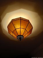 Side angle view of the stained glass ceiling fixture illuminated, showing the cream and amber colored panels and decorative metal diffuser at the base.