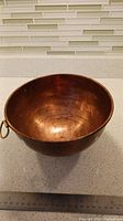 Top view of a copper mixing bowl showing the inside surface and patina, placed on a speckled countertop with ruler for size reference.