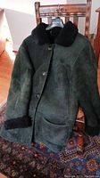 Front view of vintage black suede and shearling coat hanging on chair, showing button closure and shearling details on collar and cuffs