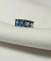 Front view showing four square-cut blue stones set side by side in gold prongs