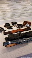 Photo showing all 8 women's leather belts in various colors and buckle styles laid out on counter
