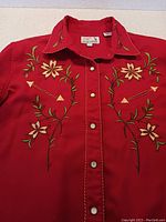 Front view showing red cowboy shirt with detailed floral embroidery, pearlized snap buttons down the center, and stitched trim on collar and front placket.