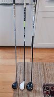 Three fairway woods showing club heads, shafts, and grips (TaylorMade RBZ, TaylorMade Burner, Callaway Big Bertha Steelhead Plus). The grips are white and black, showing minimal wear, shafts mostly black with branding details.