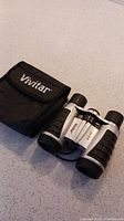 Vivitar binoculars with black rubber grips beside black carrying case on white surface