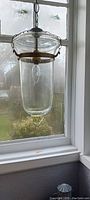 Full view of the vintage pendant lamp hanging in front of a window, showing clear glass and brass band at the top