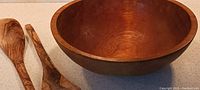 Close-up of large wooden bowl and two handcrafted burl wood salad tongs showing detail of wood grain and shape.