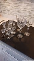 Full set of 11 Waterford crystal glasses displayed on a black countertop showing different sizes and styles.
