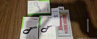 Three Apple AirTags in Belkin holders with straps, displayed alongside a pink Apple Watch band in original packaging and a permanent marker for scale.