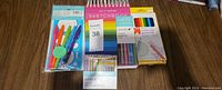 Art supplies including sketchbook, colored pencils, markers and pens arranged on wooden floor