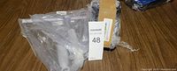 Two transparent bathroom shower squeegees with white handles lying on a wooden floor, packaged in plastic bags.