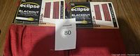 Two packages of Eclipse blackout curtains in red color, showing folded curtains and packaging with label.
