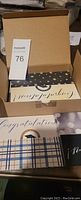 Photo showing the open box containing multiple greeting cards in various designs including one with gold text on black and star pattern, and some striped styles.