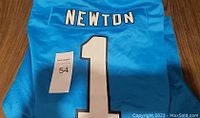 Back view of Carolina Panthers blue jersey with "Newton" and number "1" printed on back, size tag and condition visible