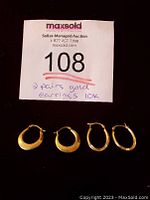 Four gold hoop earrings laid next to auction lot number card on black background