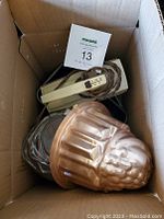 View of box with vintage Sunbeam hand mixer, copper-tone jelly mold, and metal baking pans packed inside.