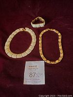 Three Butler signed costume jewelry pieces: one cream-colored bracelet, one gold-tone bracelet, and one gold-tone necklace displayed on a dark background with measurement cards