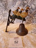 Mother Goose cast iron dinner bell wall decor shown upright against a lace curtain background, displaying the three goose figures mounted above the bell and the mounting bracket on the side.