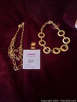Two gold-tone chain link necklaces laid on dark fabric with seller tag. Monet necklace with oval links and Anne Klein necklace with circular links shown.