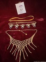 Three costume jewelry necklaces displayed on red fabric background with measurement tape for scale.