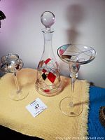 Front view of the vintage hand painted decanter with stopper and two candle holders on a yellow cloth, showing design and shape.