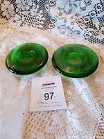 Two green glass candleholders set on lace fabric, showing top view and overall shape