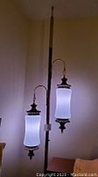 Full view of tension pole lamp with two lit ribbed glass shades reaching ceiling