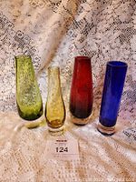 Full front view of four multicolored Scandinavian Sommerso style glass vases, green, amber, red, blue, on lace background with lot number card.