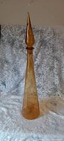 Full height view of amber Empoli glass genie bottle with stopper on lace background.