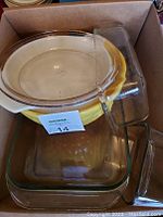Box containing multiple Pyrex glass mixing bowls and glass baking dishes, stacked with the yellow bowl visible in the middle.