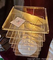 Front angled view of plexiglass rotating display carousel showing five square tiers with slots and a round spinable base.