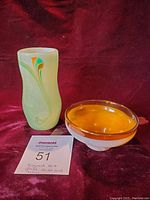 Photo showing a greenish hand blown vase with colorful swirls next to an amber glass bowl, both signed JDB.