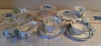 Six teacups and matching saucers arranged on a tablecloth, showing different floral patterns and gold accents.