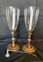 Pair of hurricane candle sticks with clear glass shades, wood bases and brass fittings, accompanied by a candle snuffer.