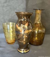 Photo shows three vintage brown amber glass items including a bottle, tumbler, and floral decorated vase.