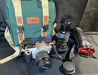 Canon EOS Rebel 2000 camera with Canon 28-80mm lens, Vivitar 75-205mm lens, Hoya Skylight filter pouch, body cap, and green Canon bag displayed on black surface.