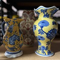 Photo showing three vases: yellow chinoiserie floral ruffled top vase, orange pitcher-shaped floral vase, and taller orange brocade triangular vase.