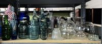 Wide view of assortment of clear and colored glass bottles, vases, jars, and glassware on shelf