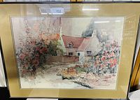 Front view of the framed watercolor painting showing the cottage surrounded by flowers with a mat and gold frame.