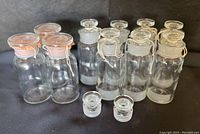 Ten clear glass apothecary jars with glass stoppers in two sizes grouped on black surface.